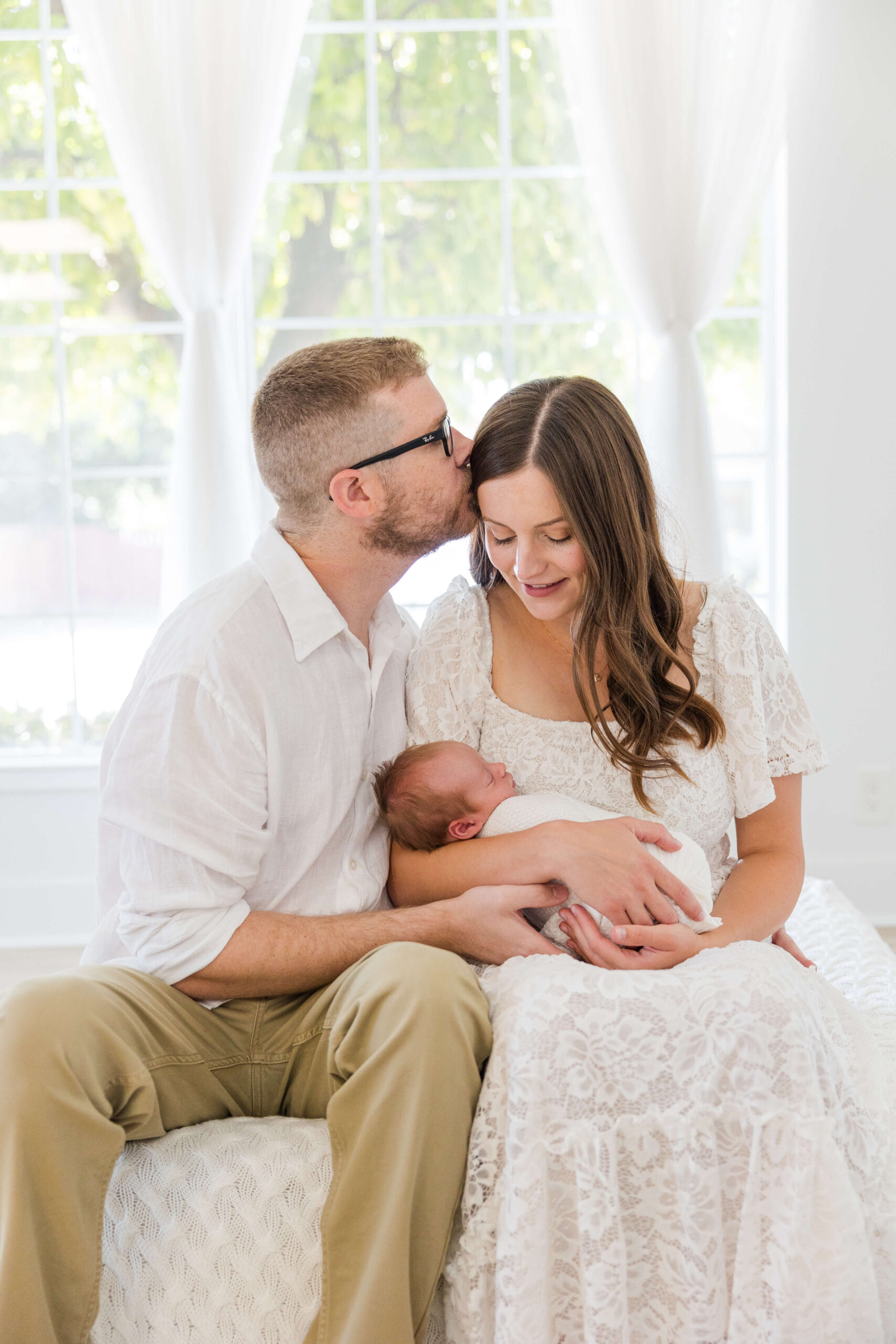 Lifestyle newborn photo with parents cuddling baby in natural light