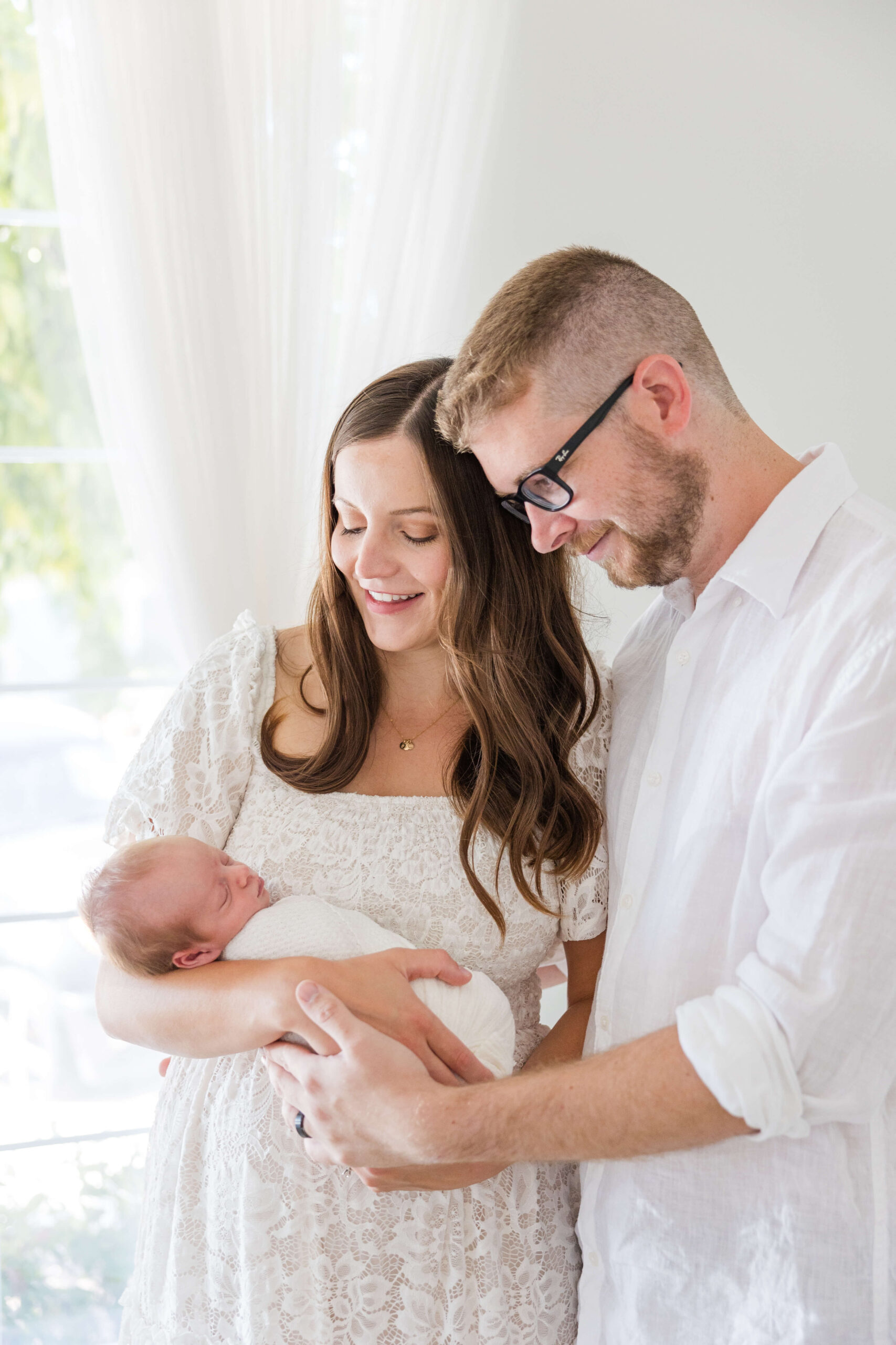 Mom and dad snuggling together looking at newborn son during studio photoshoot